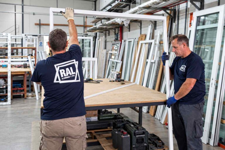 Técnicos de RAL fabricando una abertura de aluminio en taller, junto a ventanas y paneles de vidrio.